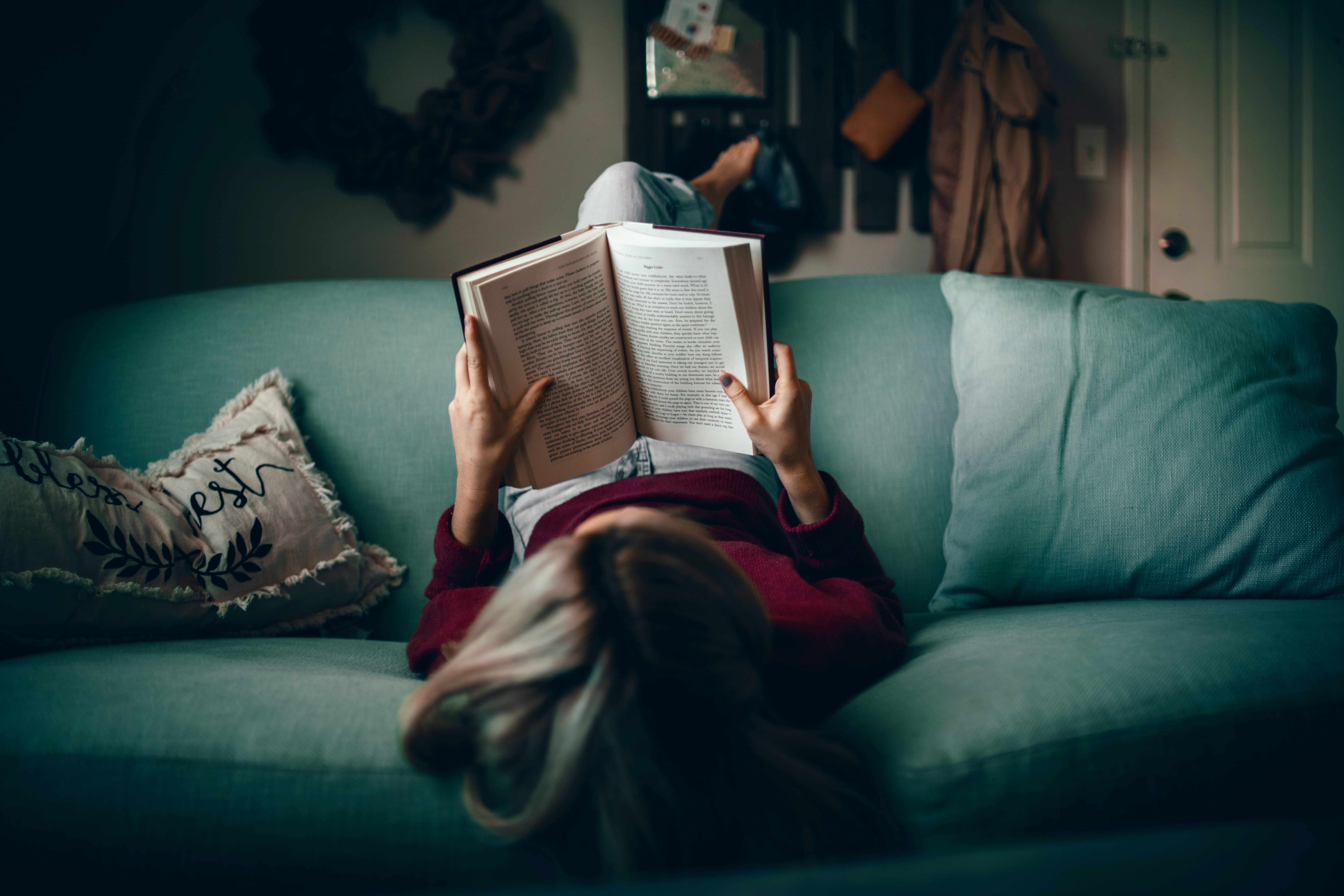 woman lying upside down on the sofa reading a book